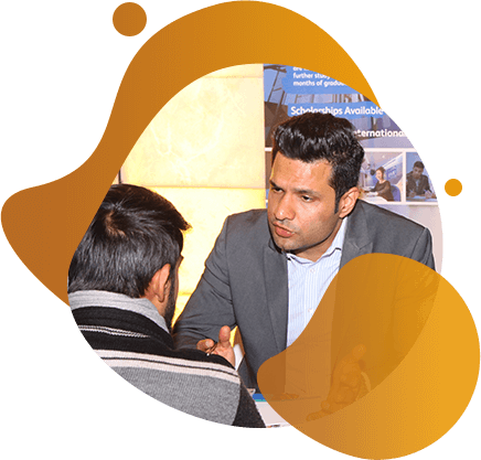 Two men engaged in a serious conversation at a table with an overseas education consultants poster in the background.