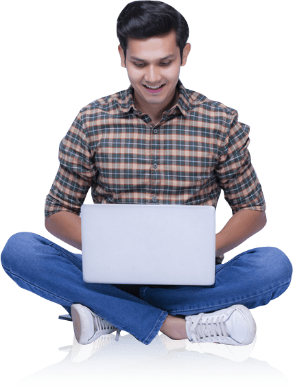 A young man in a plaid shirt and jeans sits cross-legged with a laptop on his lap, smiling as he looks at the screen, isolated on a green background.