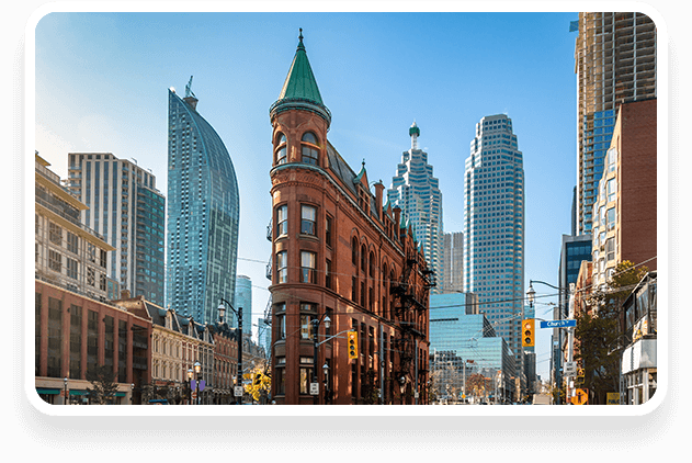 Historic red brick building with a conical roof at a street corner, surrounded by modern skyscrapers under a clear blue sky.