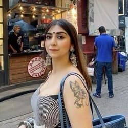 A woman with a butterfly tattoo on her arm stands in front of a food truck, smiling at the camera.