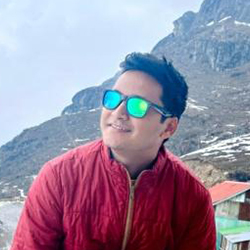 A young man in a red jacket and blue reflective sunglasses smiling in a snowy mountain landscape.