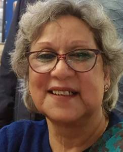 Portrait of a smiling elderly woman with gray hair and glasses, wearing a blue top.